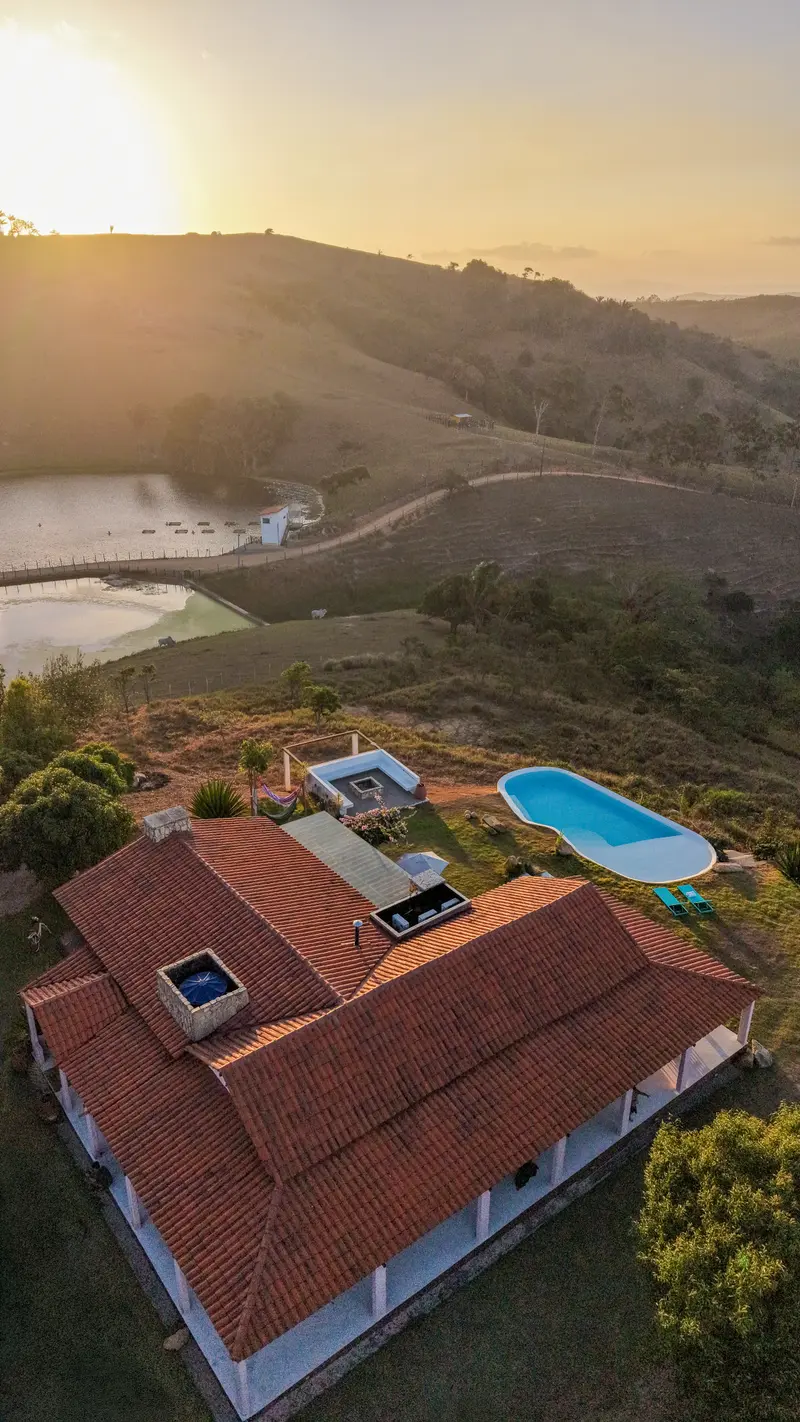 Telhado da casa em contraluz com o sol baixo e o açude ao fundo