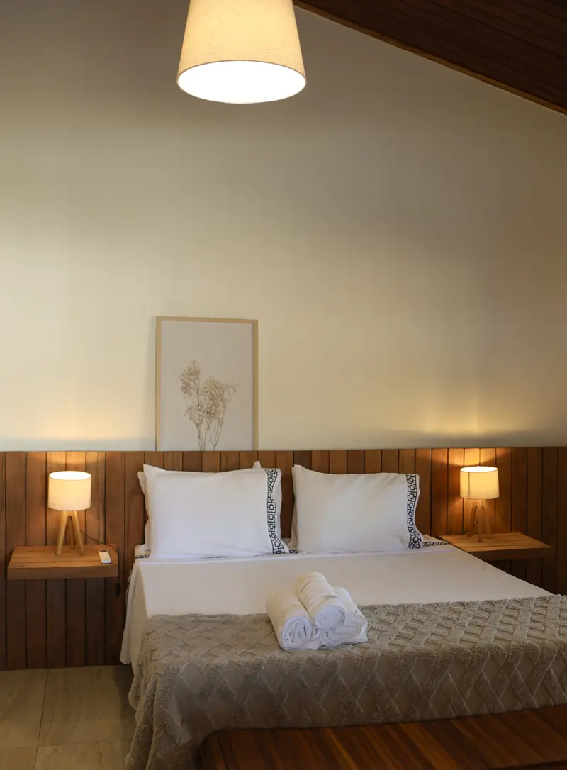 Quarto com cabeceira de madeira, abajures e roupa de cama neutra